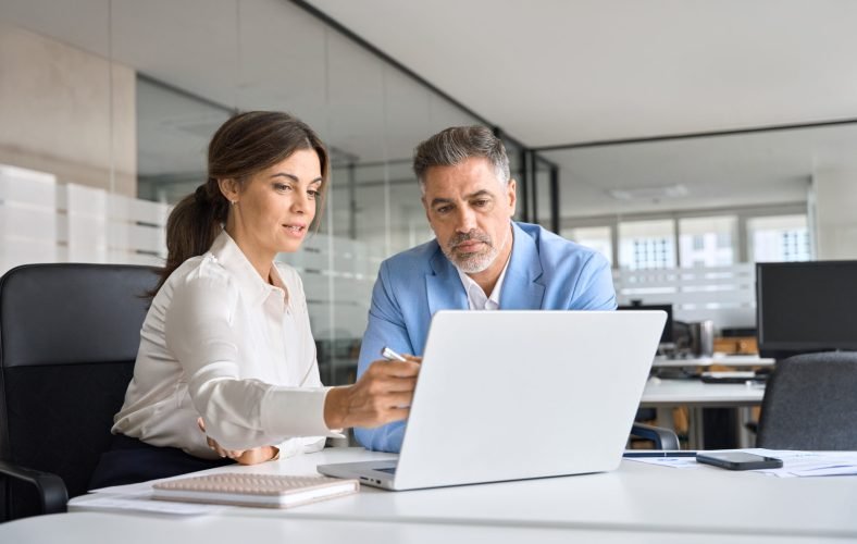 Two busy professional executive team business people working together on business finances analysis looking at computer at office meeting. Professional manager consulting corporate client using laptop